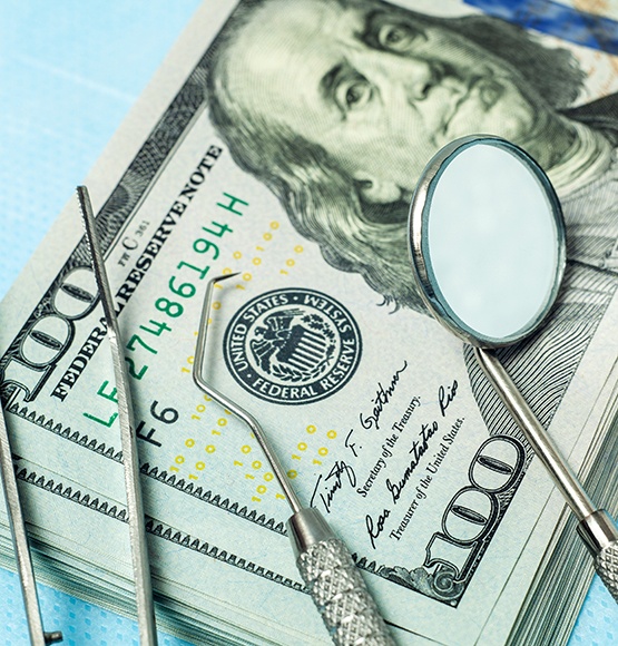 Dental tools laying on a stack of hundred-dollar bills