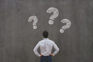 Man facing concrete wall with 3 chalk question marks above his head