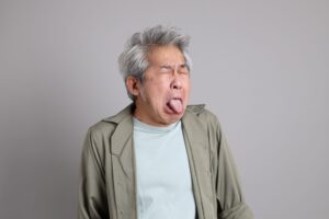 Man with gray hair in brown shirt with eyes closed sticking his tongue out